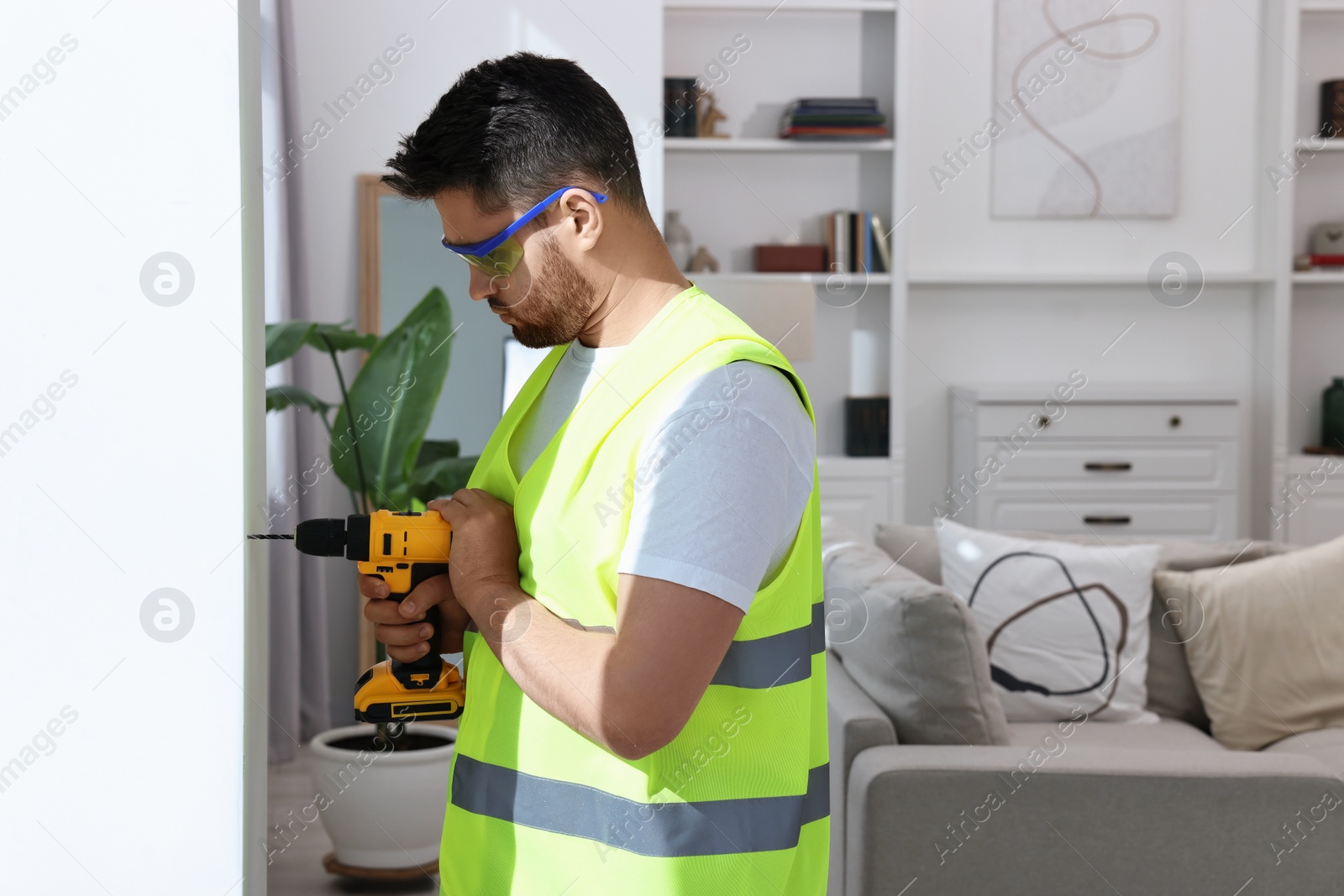 Photo of Young worker in uniform using electric drill indoors