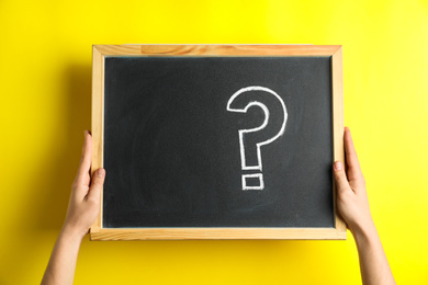 Woman holding blackboard with question mark on yellow background, closeup