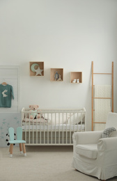 Photo of Stylish baby room interior with crib and armchair