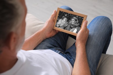 Senior man holding frame with black and white photo of his family at home, closeup