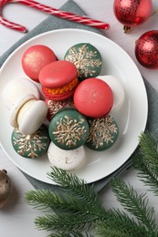 Photo of Different decorated Christmas macarons and festive decor on white wooden table, flat lay