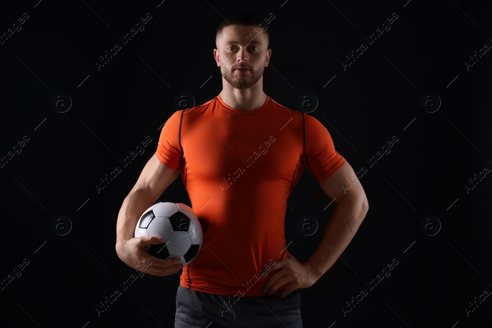 Photo of Athletic young man with soccer ball on black background