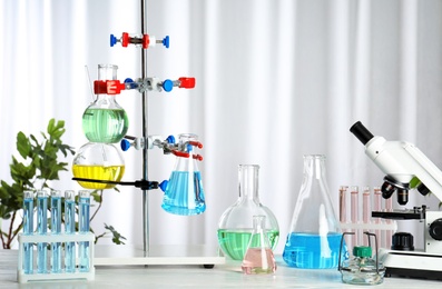 Photo of Laboratory glassware and microscope on table indoors. Chemistry concept