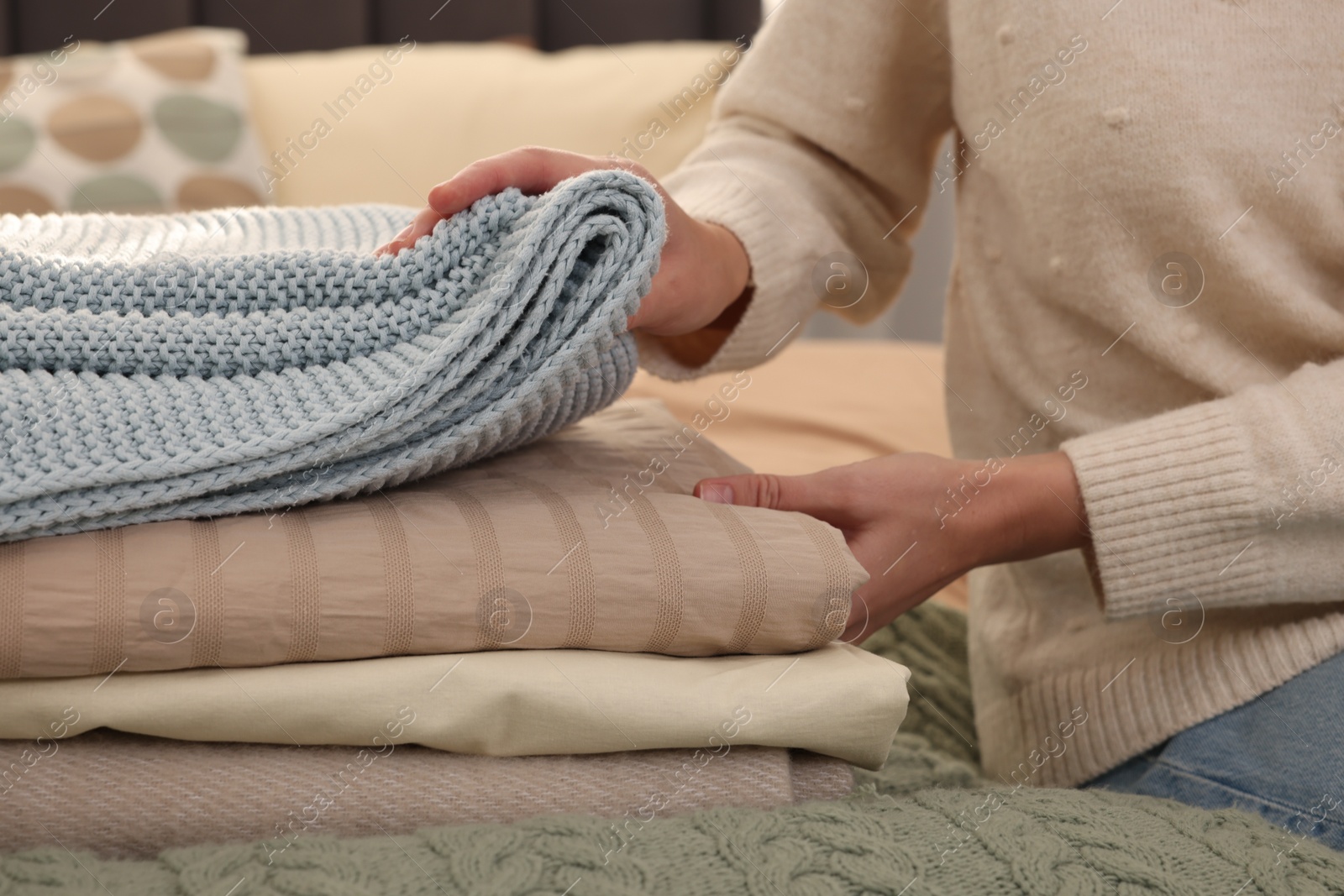 Photo of Woman with stack of different folded blankets on bed, closeup. Home textile