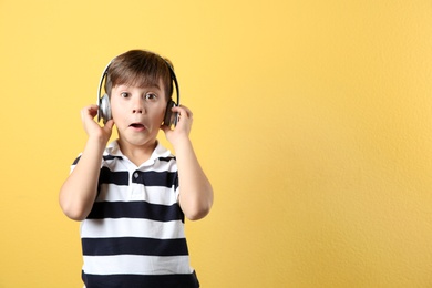 Cute little boy listening to music with headphones on color background. Space for text