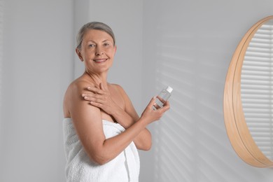 Photo of Happy woman holding bottle of body oil in bathroom. Space for text