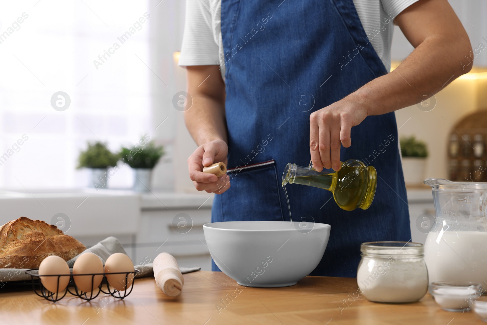 Photo of Making bread. Man pouring oil into bowl at wooden table in kitchen, closeup