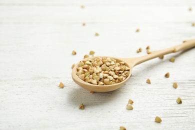 Photo of Uncooked green buckwheat grains in spoon on white wooden table