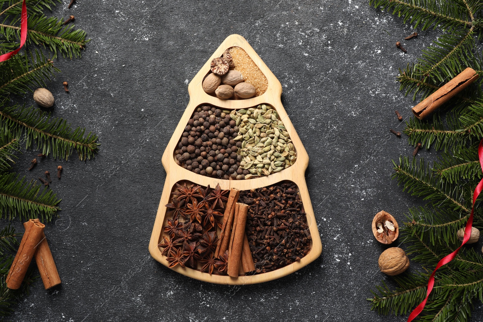 Photo of Different spices, nuts and fir branches on dark gray textured table, flat lay