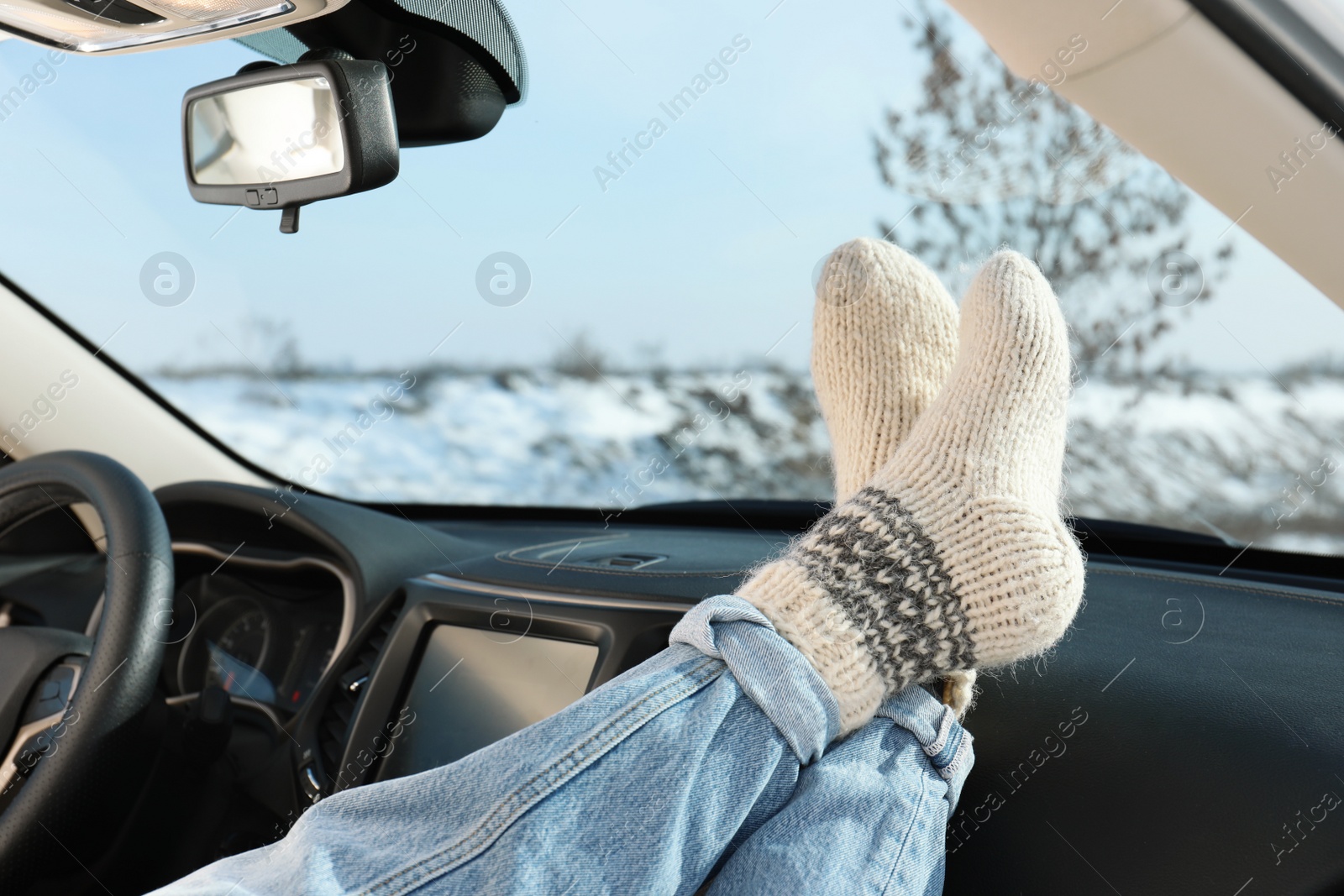 Photo of Young woman in warm socks holding her legs on car dashboard. Cozy atmosphere