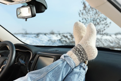 Photo of Young woman in warm socks holding her legs on car dashboard. Cozy atmosphere