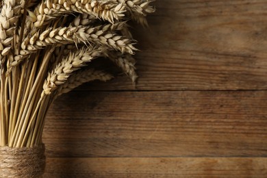 Photo of Bunch of dried wheat on wooden table, closeup. Space for text