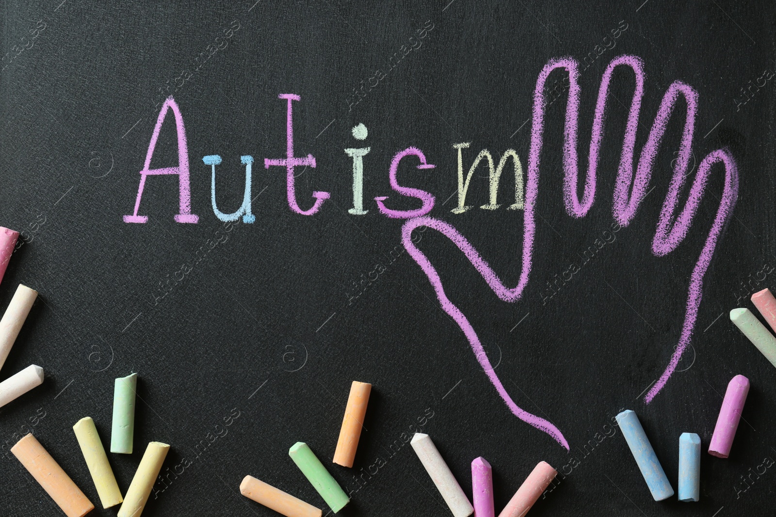 Photo of Pieces of chalk on blackboard with word Autism and drawn palm, flat lay