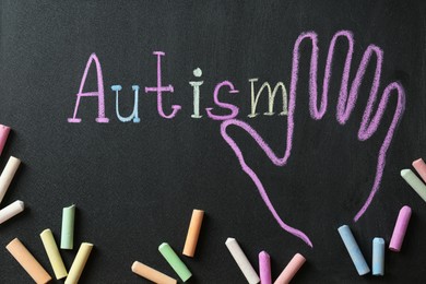 Pieces of chalk on blackboard with word Autism and drawn palm, flat lay