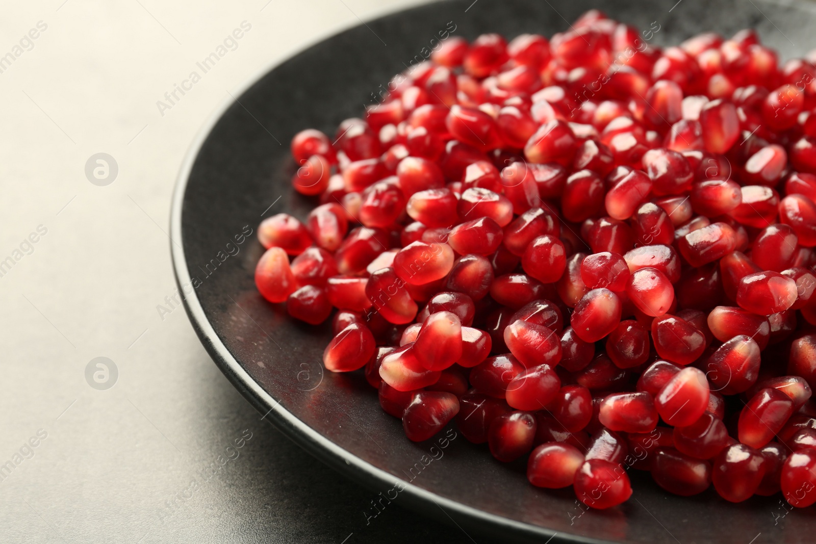 Photo of Ripe juicy pomegranate grains on grey table, closeup