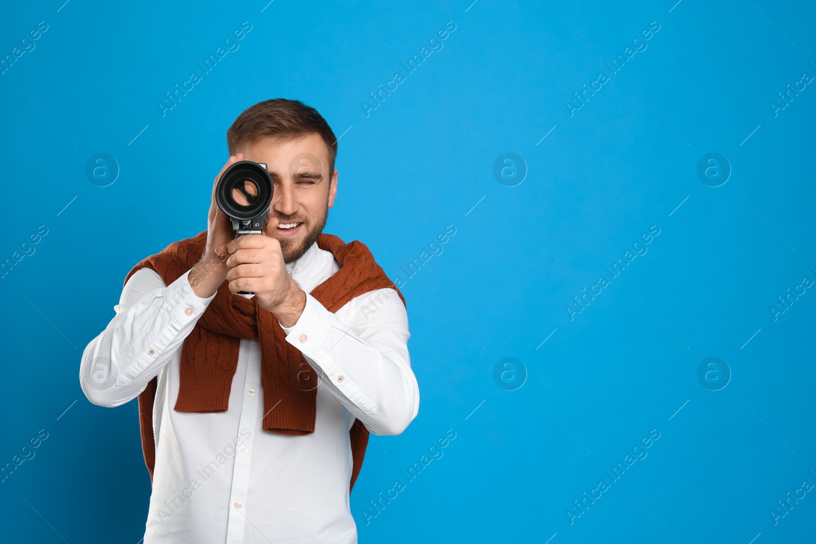 Photo of Young man using vintage video camera on light blue background, space for text
