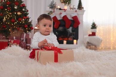 Photo of Baby with toy and gift box on floor in room decorated for Christmas