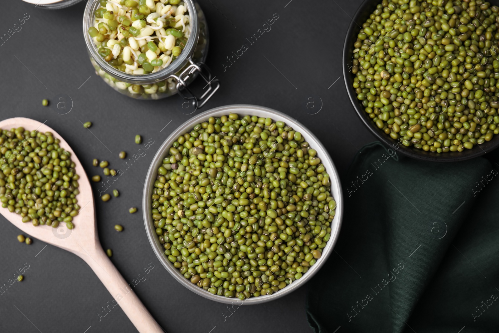 Photo of Different dishware with green mung beans on black background, flat lay