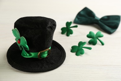 Leprechaun hat, bow tie and decorative clover leaves on white wooden table, space for text. St Patrick's Day celebration