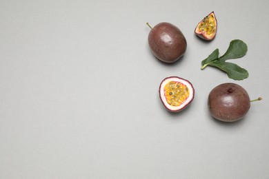 Fresh ripe passion fruits (maracuyas) with green leaf on grey background, flat lay. Space for text