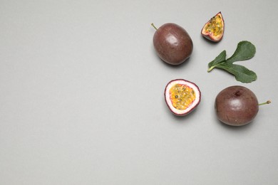 Photo of Fresh ripe passion fruits (maracuyas) with green leaf on grey background, flat lay. Space for text