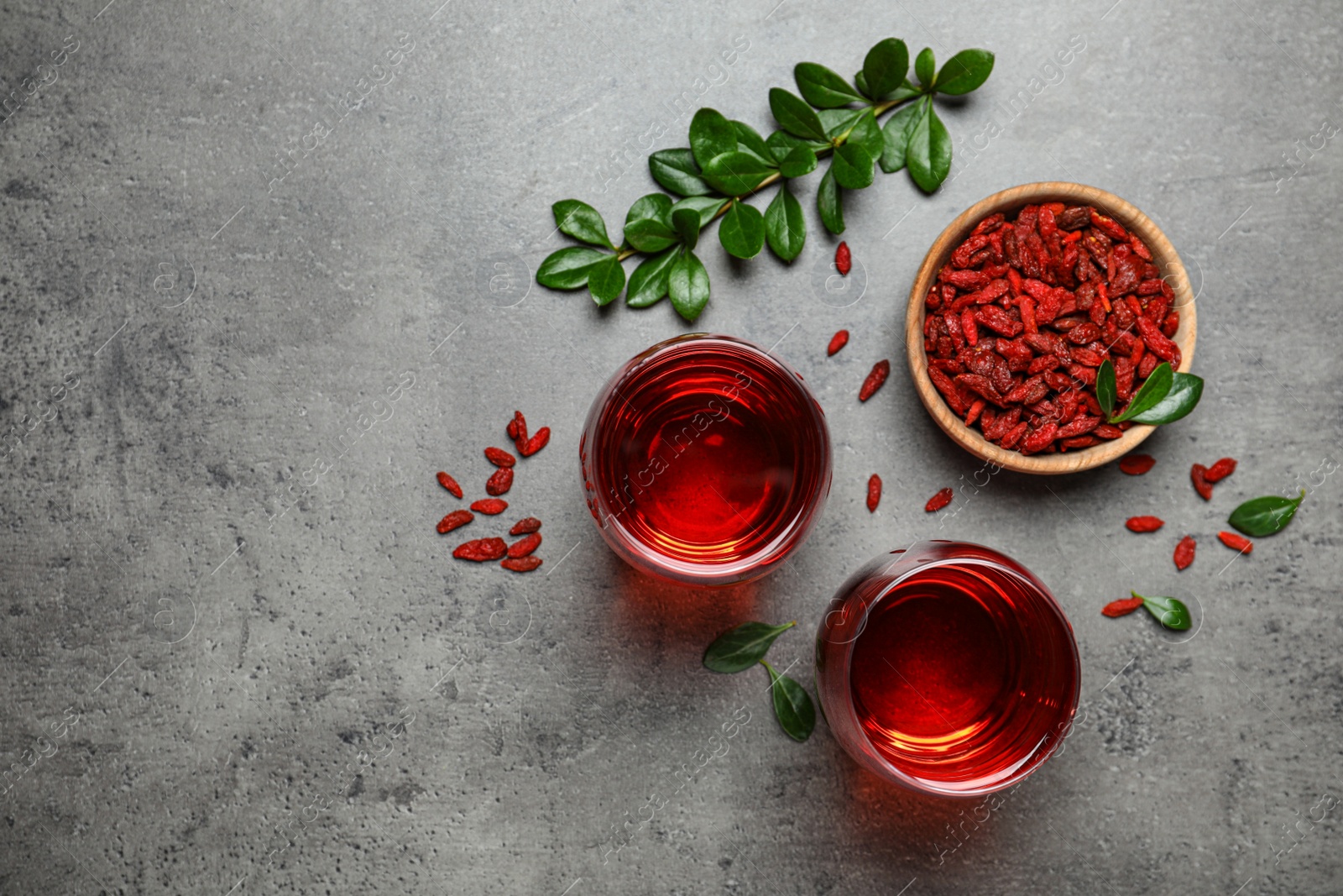 Photo of Flat lay composition with glasses of healthy goji juice on grey table. Space for text