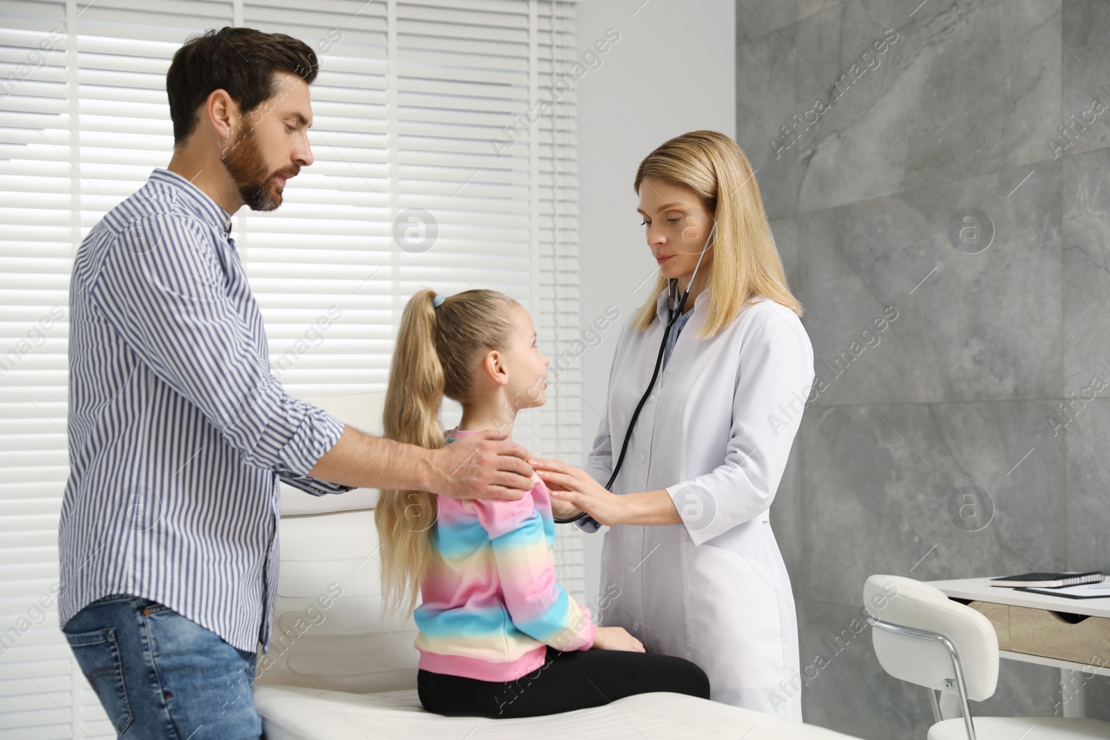 Photo of Father and daughter having appointment with doctor. Pediatrician consulting patient in clinic