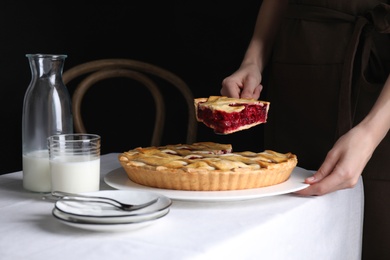 Woman taking slice of delicious cherry pie at table against dark background, closeup