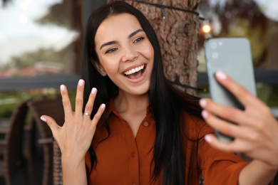 Happy woman with engagement ring taking selfie in outdoor cafe