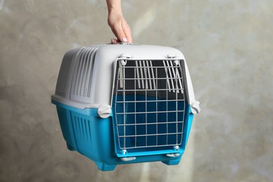 Photo of Woman holding light blue pet carrier against grey wall, closeup