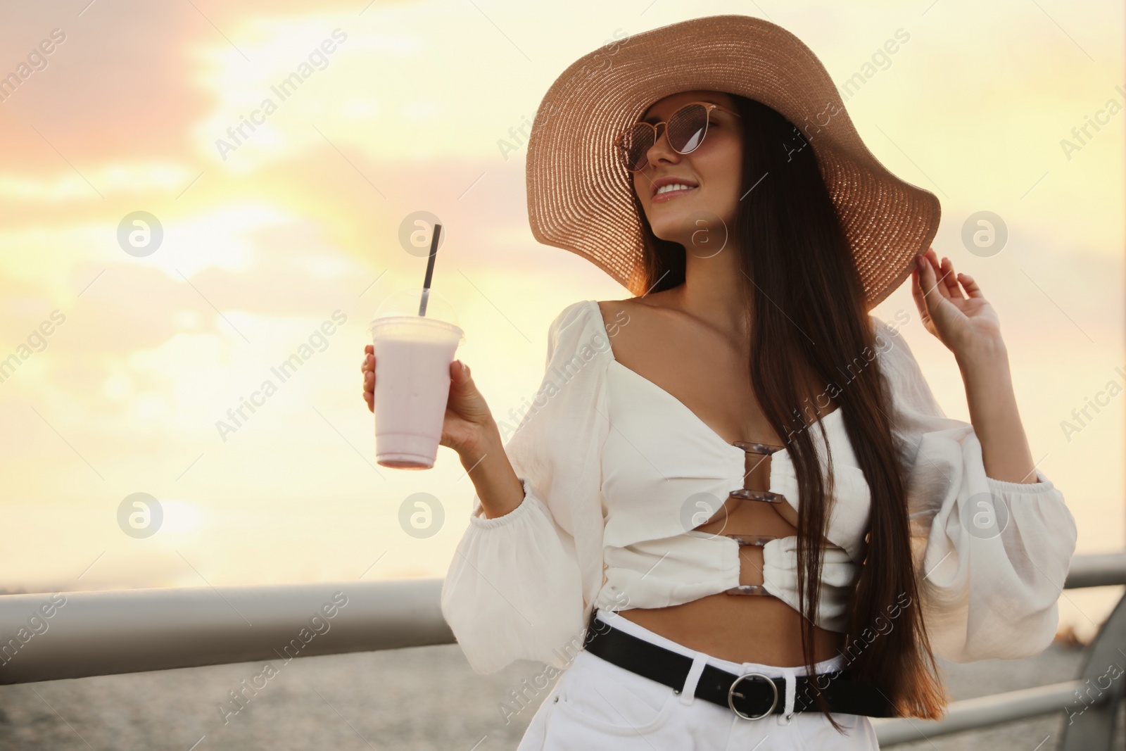 Photo of Beautiful young woman with tasty milk shake outdoors, space for text