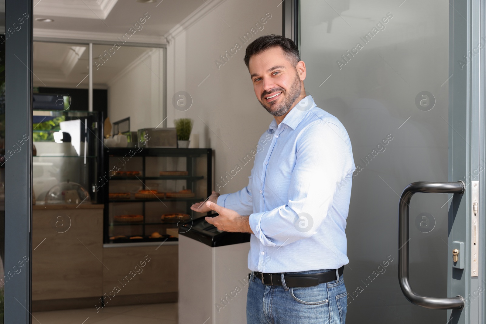 Photo of Happy business owner inviting to come into his cafe. Space for text