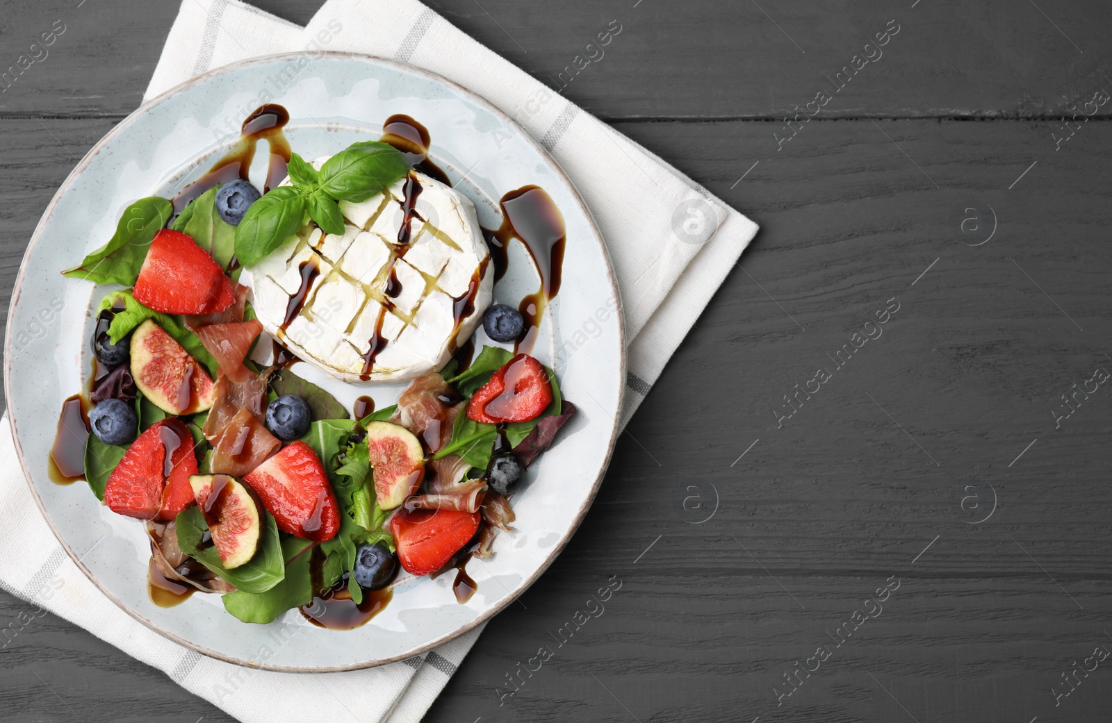 Photo of Delicious salad with brie cheese, prosciutto, berries and balsamic vinegar on grey wooden table, top view. Space for text