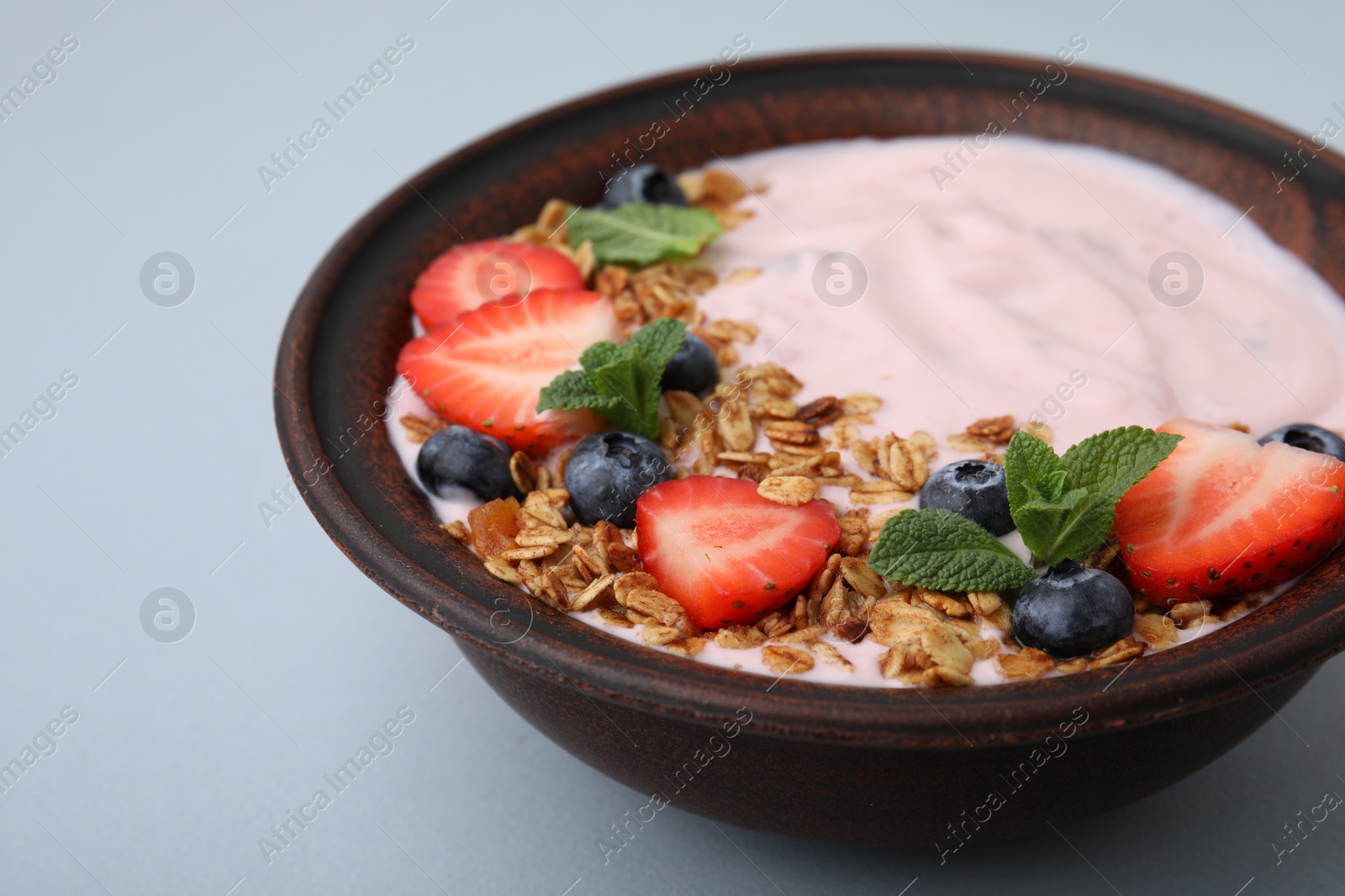 Photo of Bowl with yogurt, berries and granola on light grey background, closeup