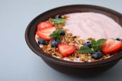 Photo of Bowl with yogurt, berries and granola on light grey background, closeup