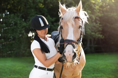 Photo of Young woman in horse riding suit and her beautiful pet outdoors on sunny day