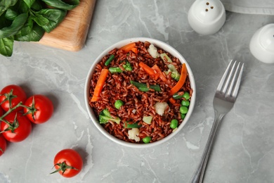 Photo of Bowl of brown rice with vegetables on grey table, flat lay