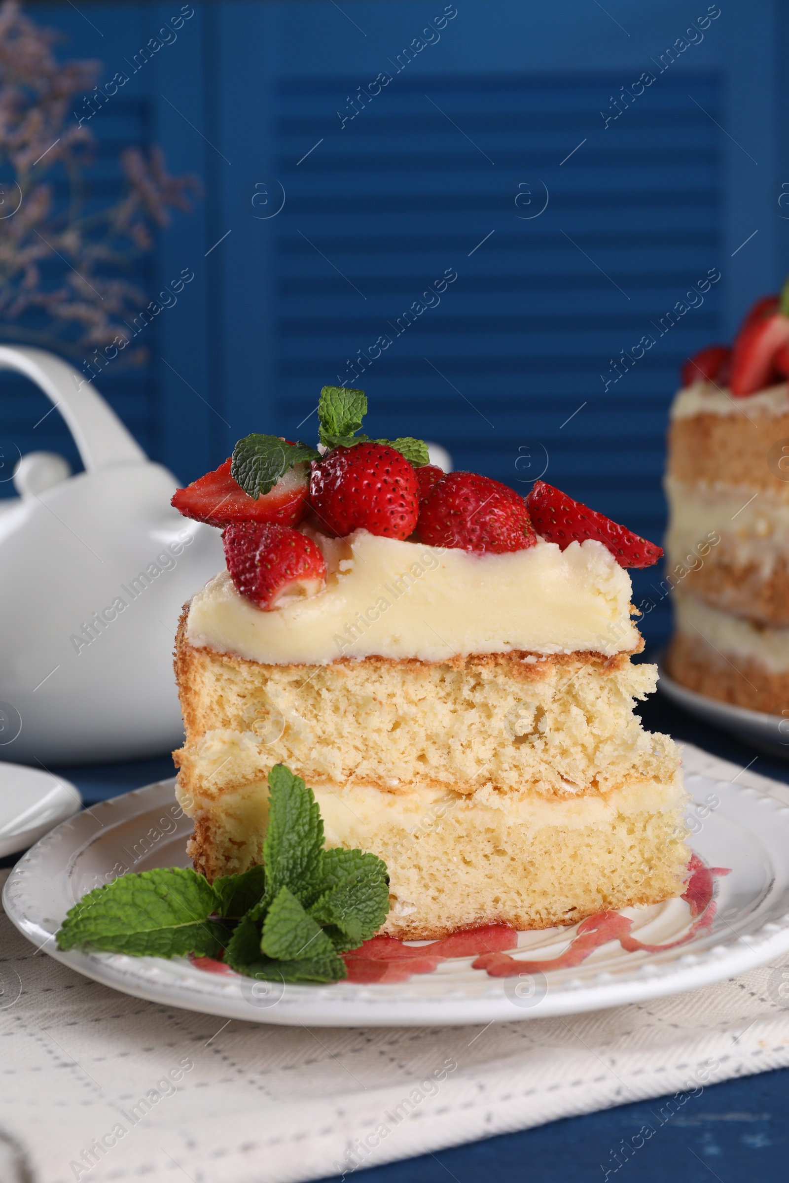 Photo of Piece of tasty cake with fresh strawberries and mint on blue wooden table, closeup