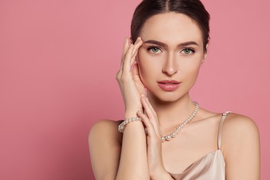 Photo of Young woman wearing elegant pearl jewelry on pink background, space for text