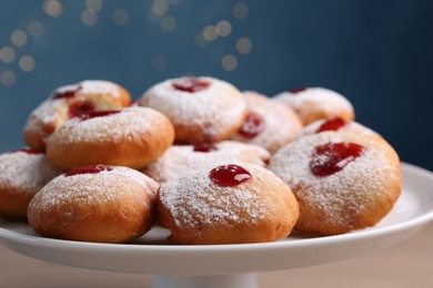 Photo of Hanukkah donuts with jelly and powdered sugar on stand against blurred festive lights, closeup