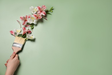 Photo of Woman holding painting brush and beautiful alstroemerias on green background, closeup. Space for text