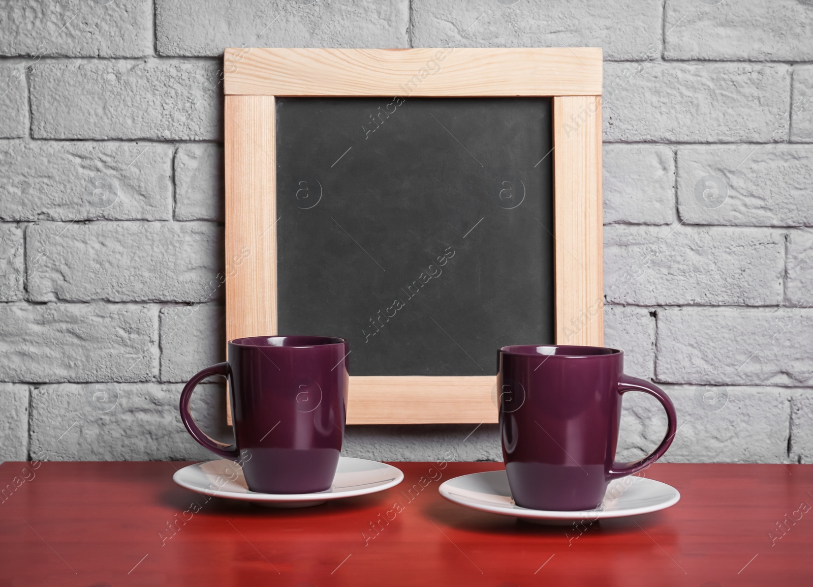 Photo of Ceramic cups on table near small chalkboard