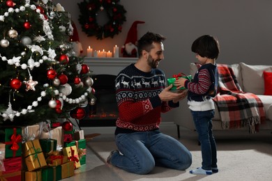 Photo of Cute son giving present to his father at home. Christmas celebration