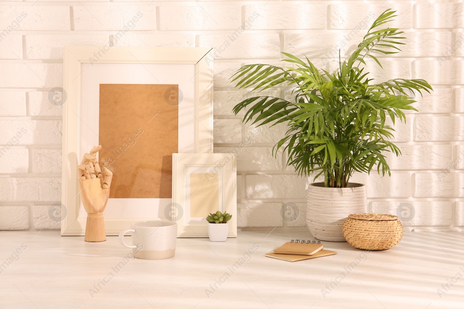 Photo of Stylish office workplace. Decor elements, plants, cup and notebooks on white table near brick wall