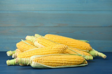 Photo of Corncobs with husks on blue wooden table. Space for text