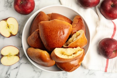 Photo of Delicious baked apple pirozhki in bowl and fruits on white marble table, flat lay