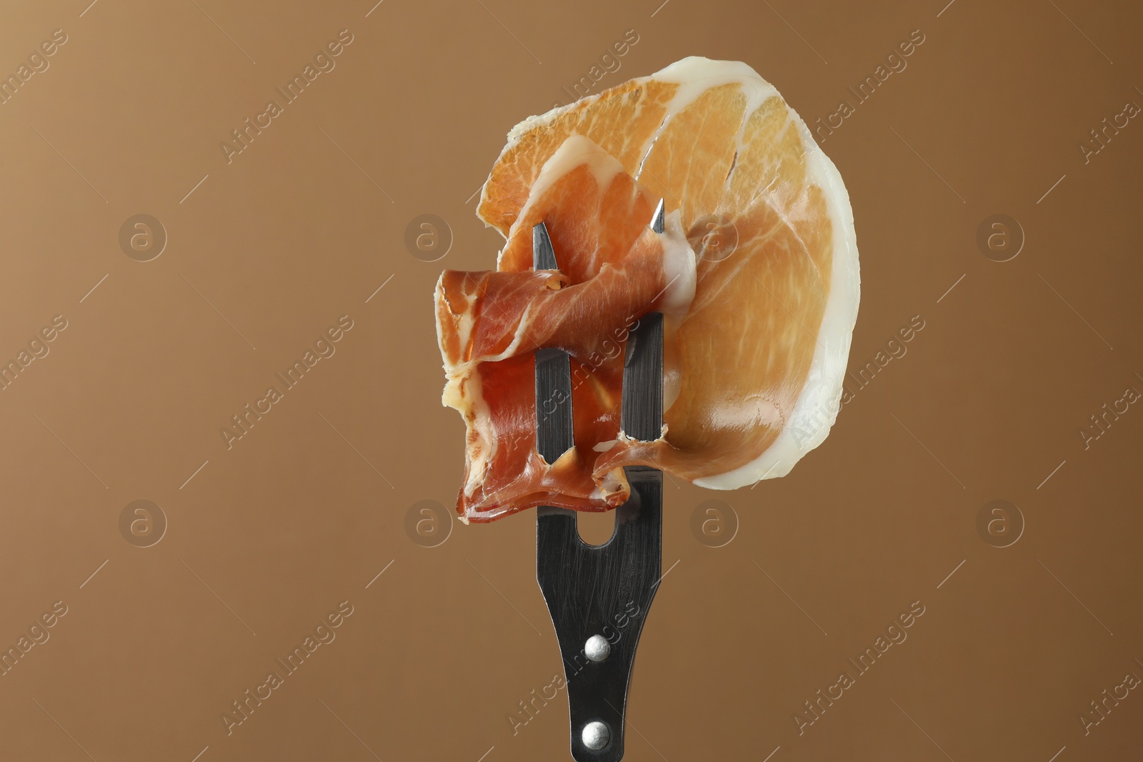 Photo of Fork with slice of tasty jamon on brown background, closeup