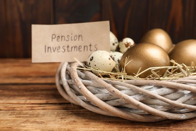 Photo of Different eggs and card with phrase Pension Investments in nest on wooden table, closeup