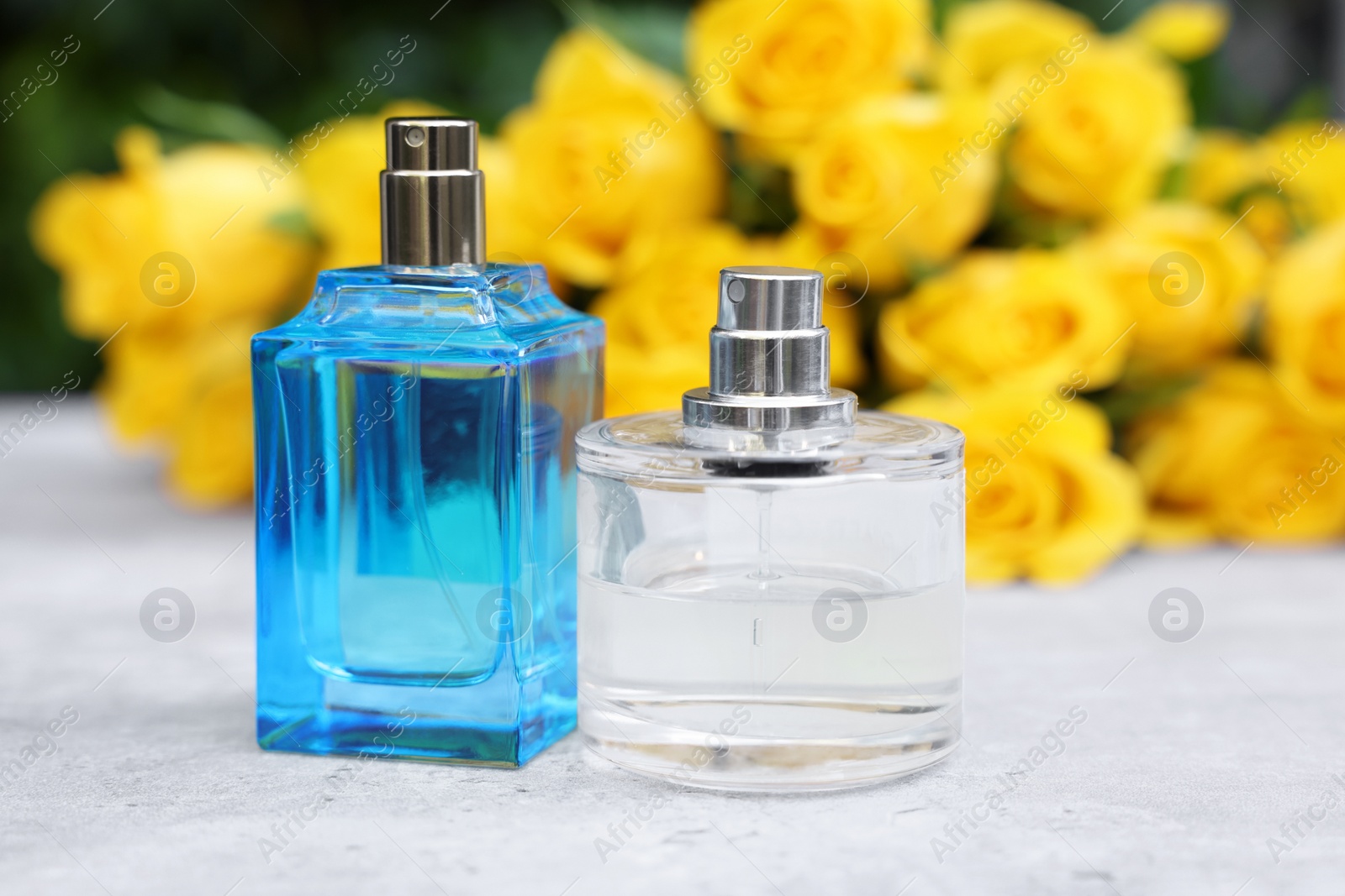 Photo of Perfumes and beautiful bouquet of yellow roses on light table, selective focus