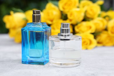 Perfumes and beautiful bouquet of yellow roses on light table, selective focus